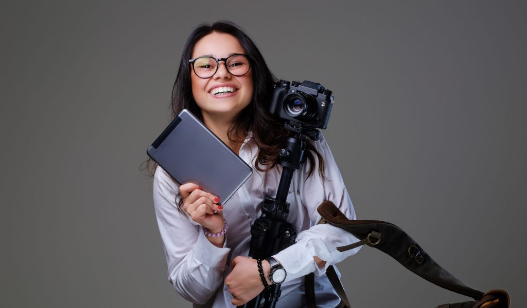 Smiling female photographer holds tripod and tablet PC.
